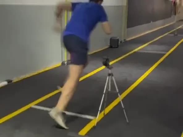 Aluno correndo no corredor de sprint com o sensor Vektor Speed no tripé em primeiro plano